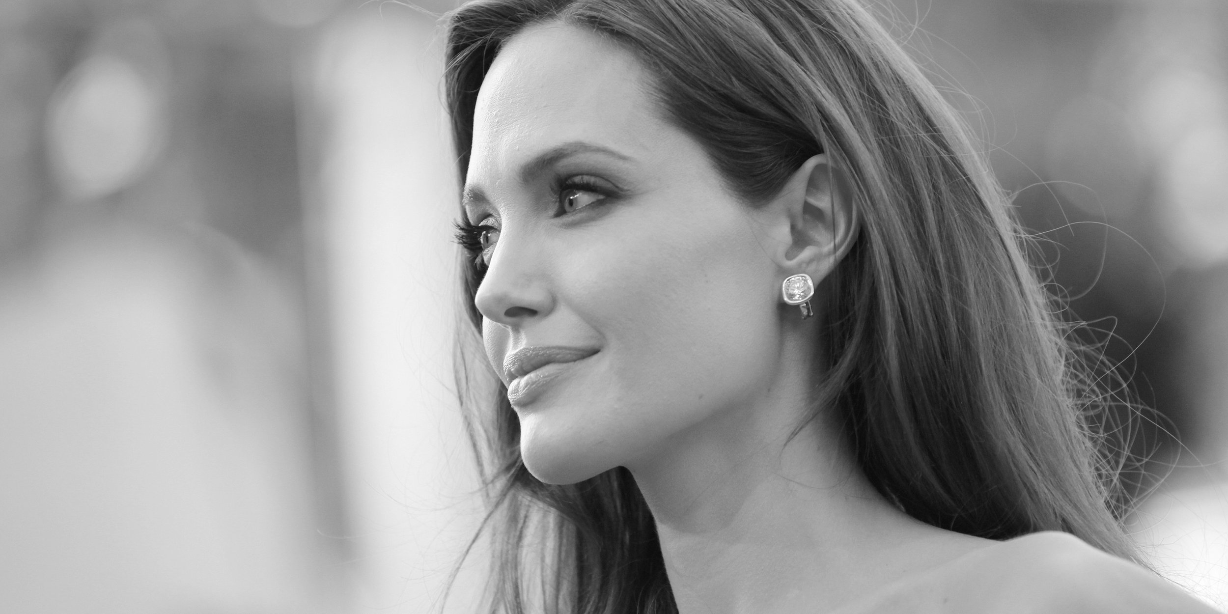 Black and white portrait of a woman with long hair and earrings, gazing to the side.