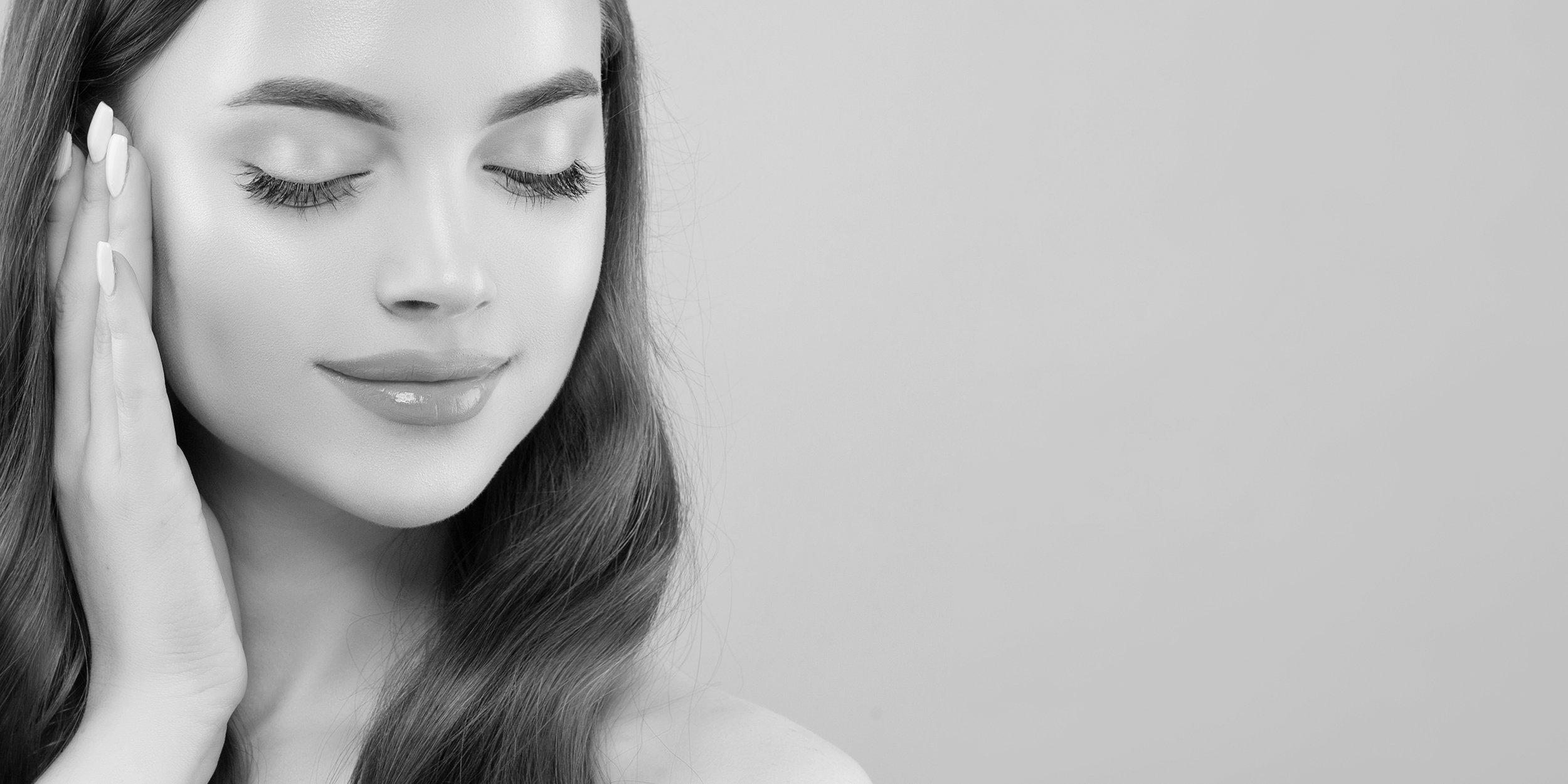 Black and white photo of a woman with closed eyes touching her face, smiling softly.