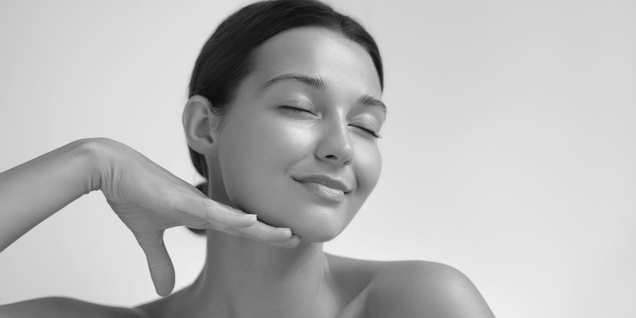 Black and white photo of a woman with closed eyes smiling, holding her hand under her chin in a relaxed pose.