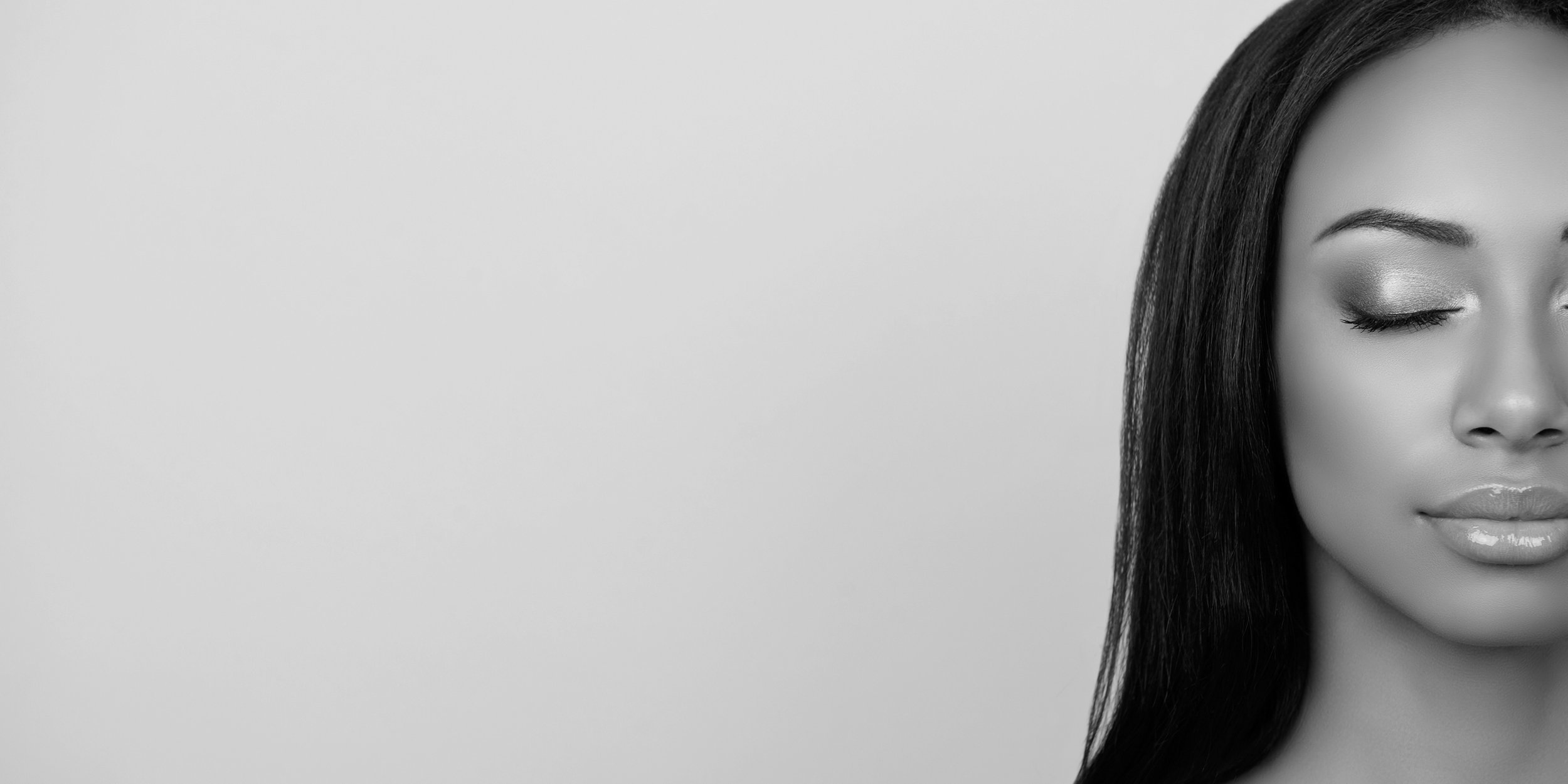 Close-up of a woman's face with her eyes closed, showing her makeup, black hair, and smooth skin, in black and white.