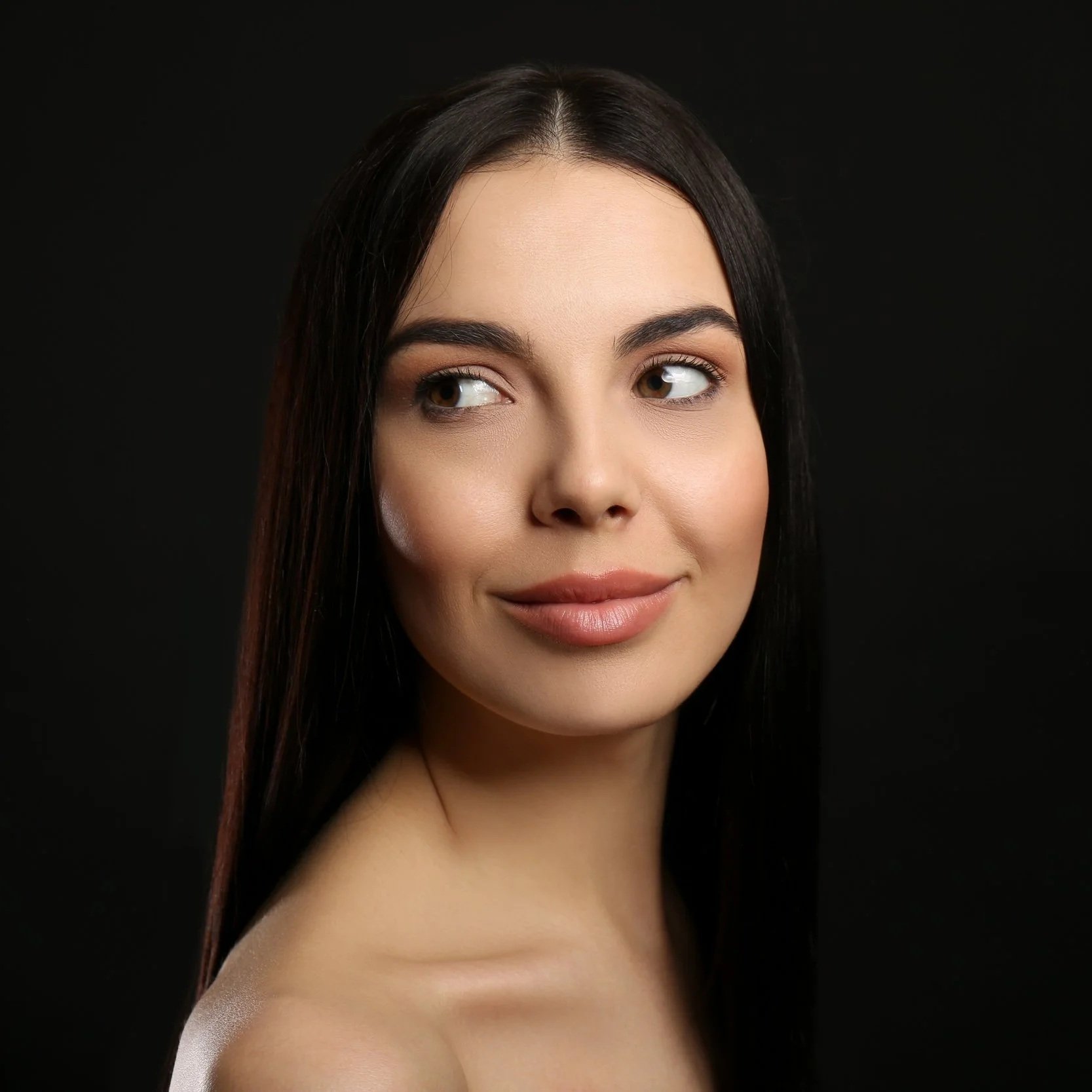 Close-up portrait of a young woman with long dark hair, looking to the side, with a neutral expression, against a black background.