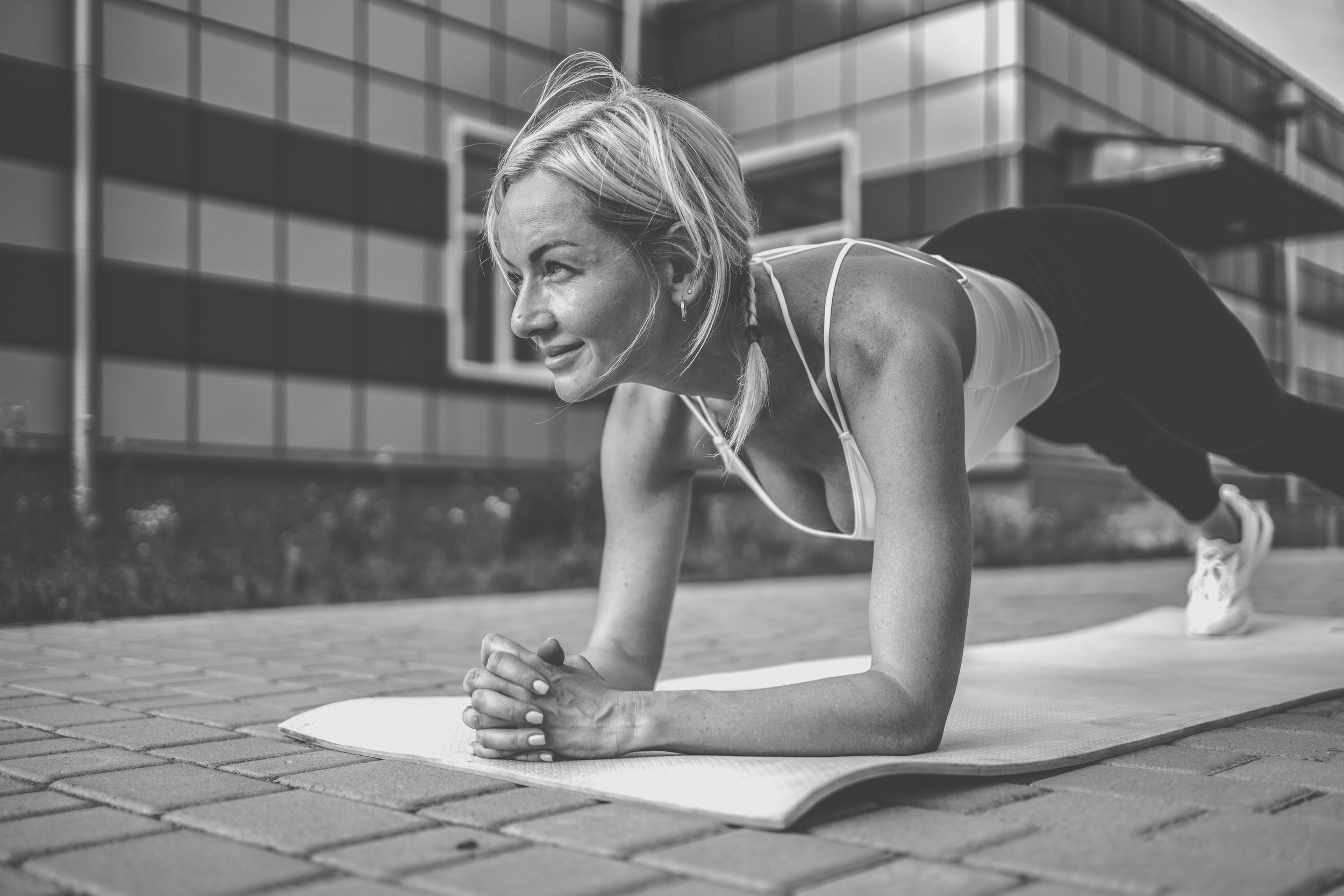 Woman doing plank exercise outdoors on a yoga mat in front of a modern building.