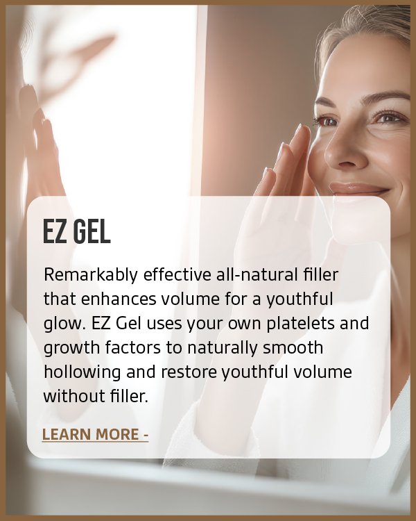 A smiling woman looking at her reflection in the mirror while applying skincare to her face.