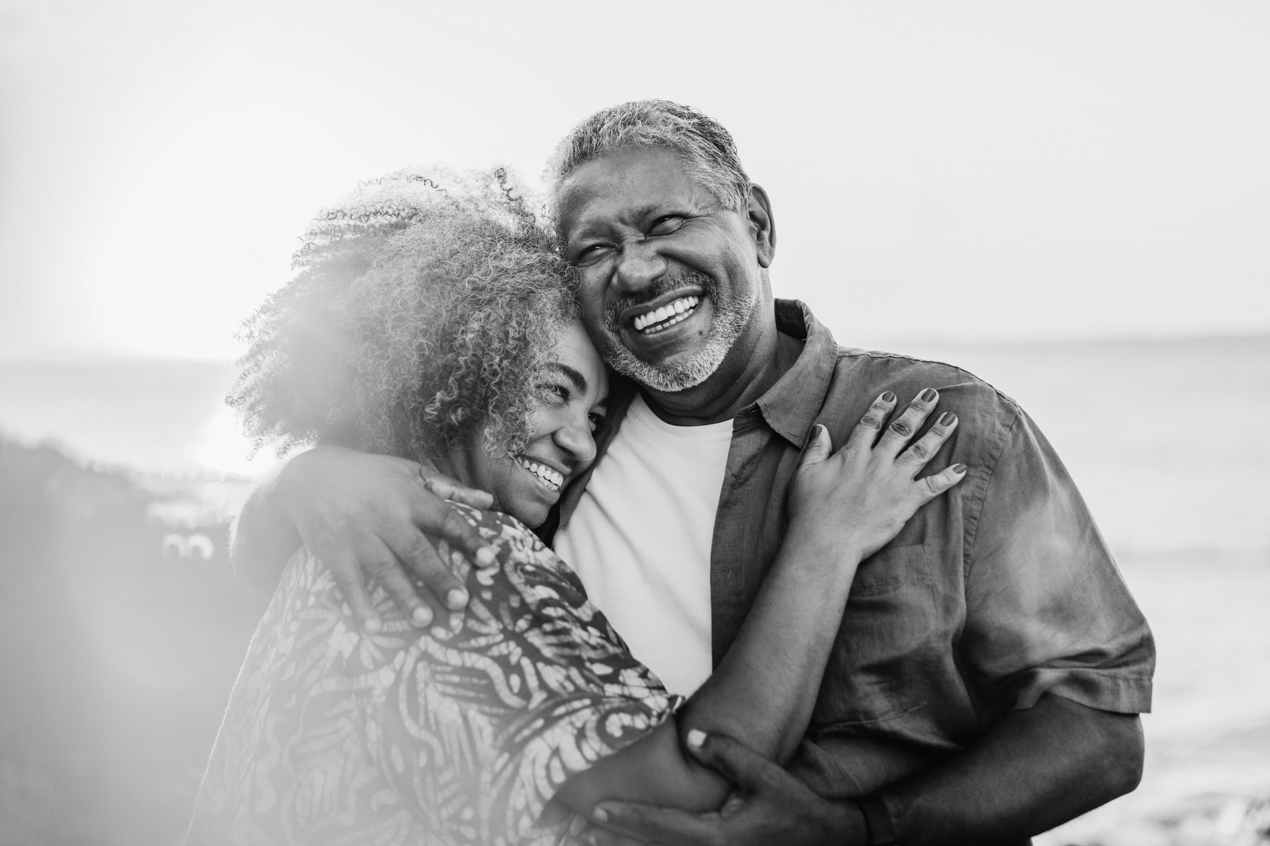 A happy middle-aged couple hugging on the beach, smiling and enjoying each other.
