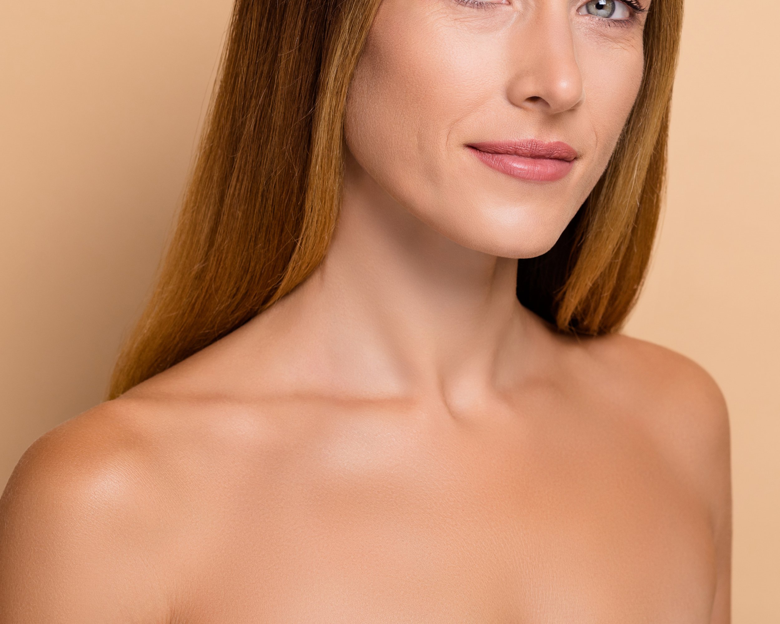 Close-up of a woman with fair skin and long red hair, showing her shoulder and part of her face, with a neutral beige background.
