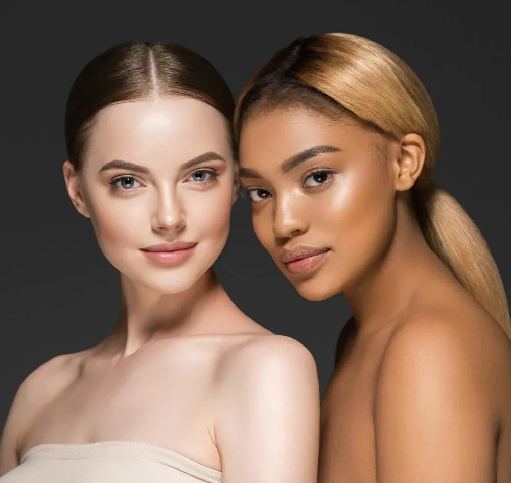 Two women with different skin tones and hair colors posing closely against a dark background.