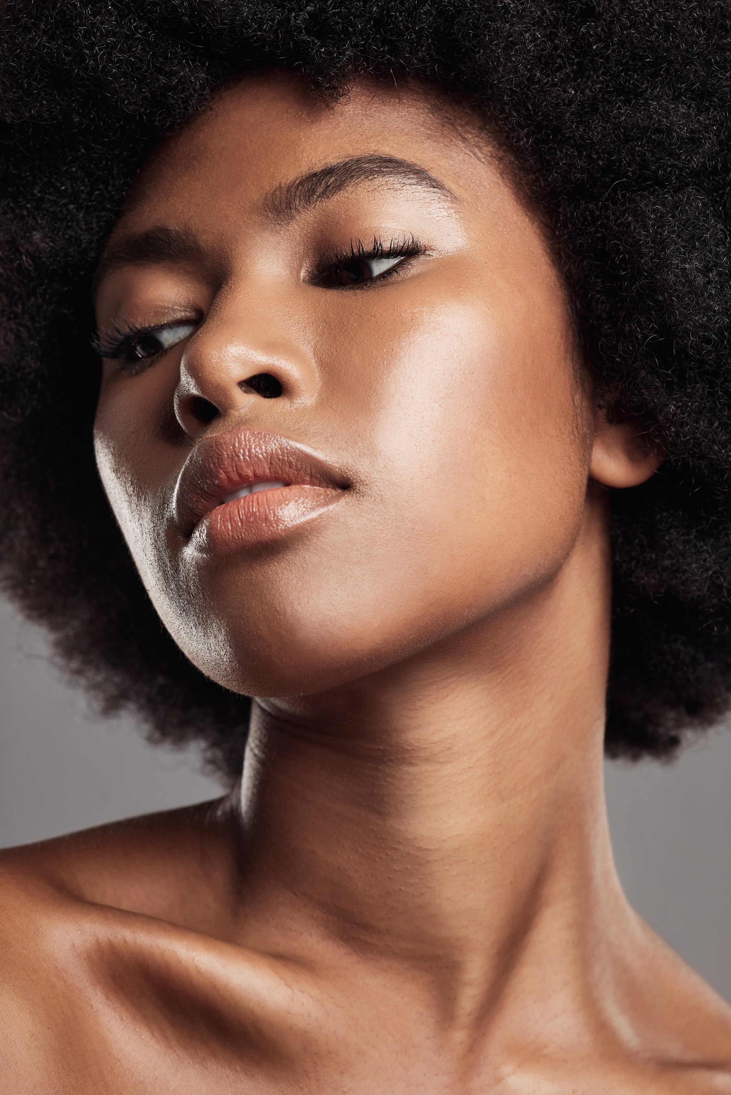 Close-up of a young Black woman with natural curly hair, smooth skin, and neutral makeup.